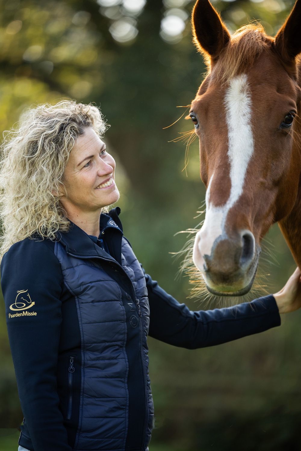 Een vrouw kijkt glimlachend naar Gorgeous en houdt haar hand bij de neus van het paard.