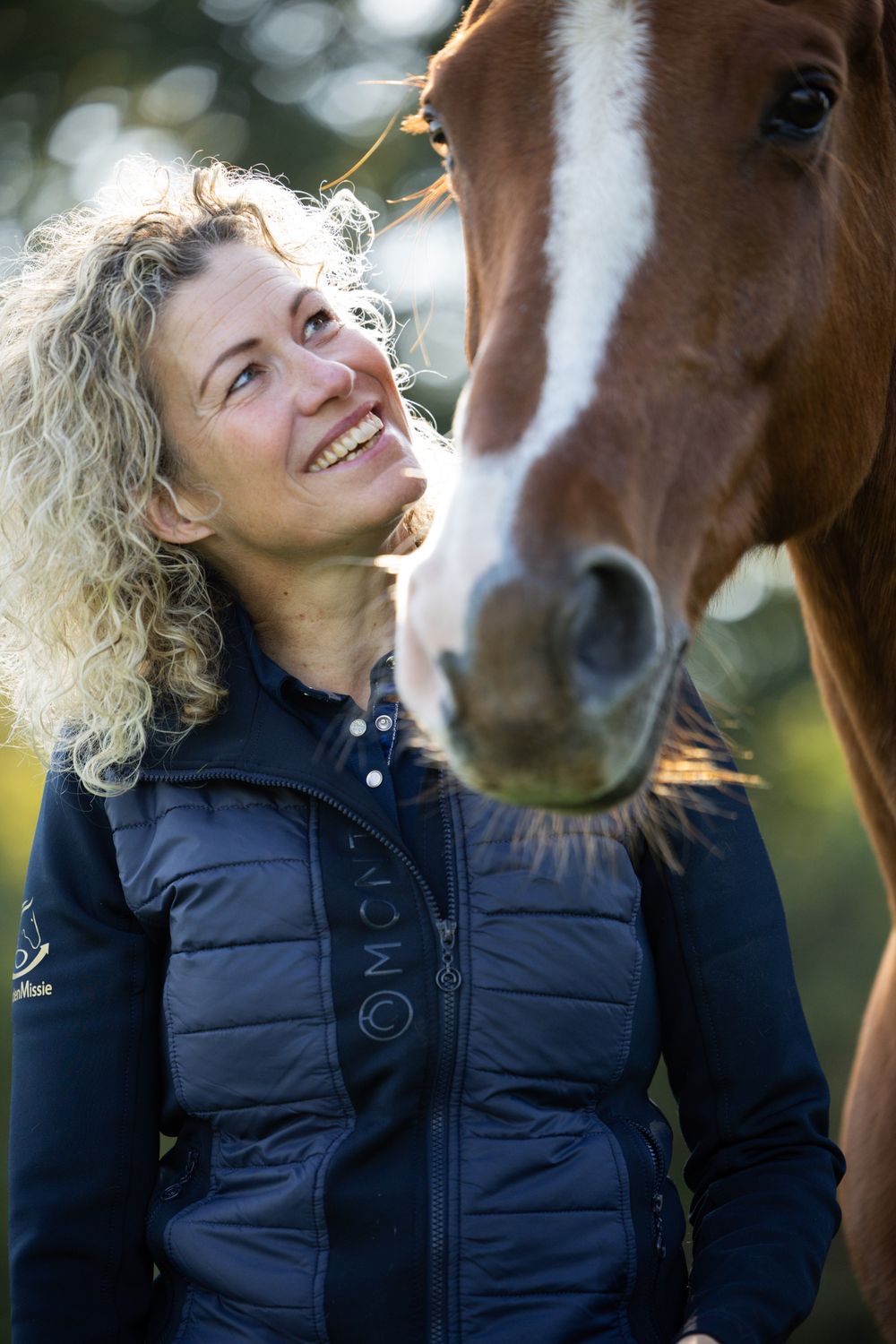 Een vrouw met blonde krullen kijkt lachend omhoog naar Gorgeous.