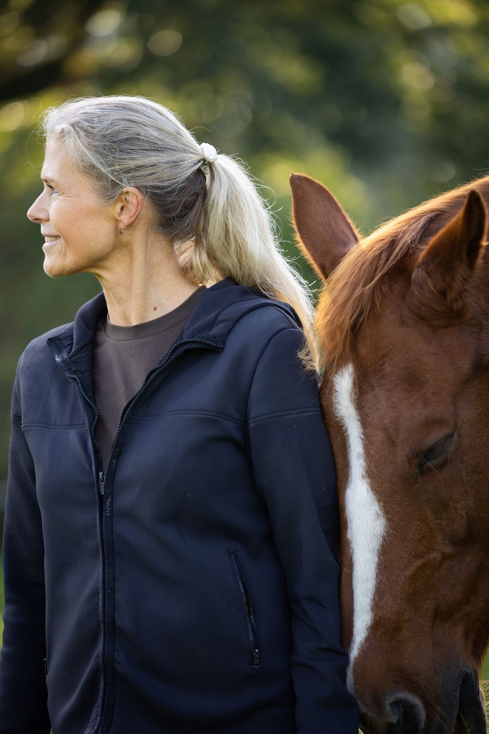 Een vrouw kijkt ontspannen opzij terwijl Gorgeous naast haar met gesloten ogen staat.